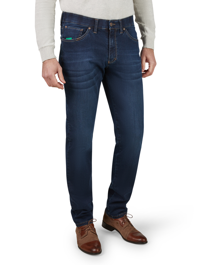 Herren in dunkelblauen Jeans mit geradem Schnitt, seitlichen Taschen und sichtbaren Nähten, getragen mit braunen Lederschuhen und einem grauen Pullover.