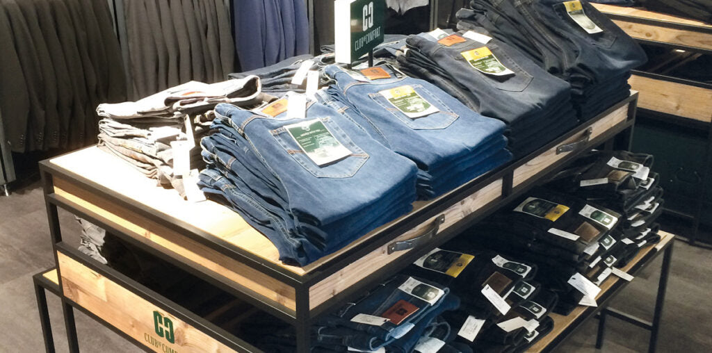 Blaue, graue und schwarze Jeanshosen sind auf einem Ladenregal in einem Bekleidungsgeschäft stapelweise gefaltet und mit Preisschildern versehen.