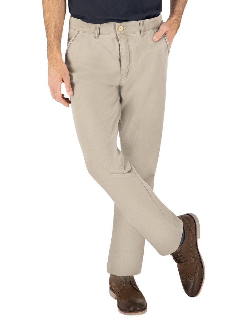 Hände in den Taschen, trägt beige Chino-Hose und braune Lederschuhe, die zu einem dunkelblauen Hemd passen, in einer entspannten Pose mit einem Bein leicht vorgestreckt.