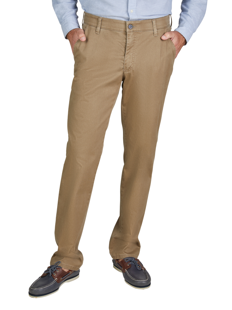 Bauchbedeckende, beige Chino-Hose mit gerader Passform, zwei seitlichen Eingrifftaschen und Gürtelschlaufen. Der obere Teil einer Person ist nicht sichtbar, die Person steht mit verschränkten Händen in den Taschen, trägt ein blaues Hemd und dunkle Segelschuhe.