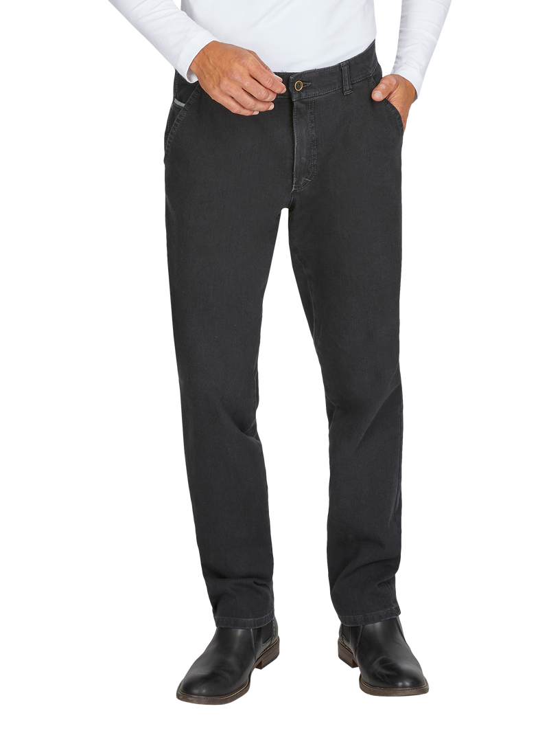 Hosenbein eines Mannes in schwarzen Jeans, er trägt ein weißes Hemd, das in die Hose gesteckt ist, eine Hand in der Hosentasche, die andere hält am Knopf, schwarze Schuhe, Hintergrund weiß.