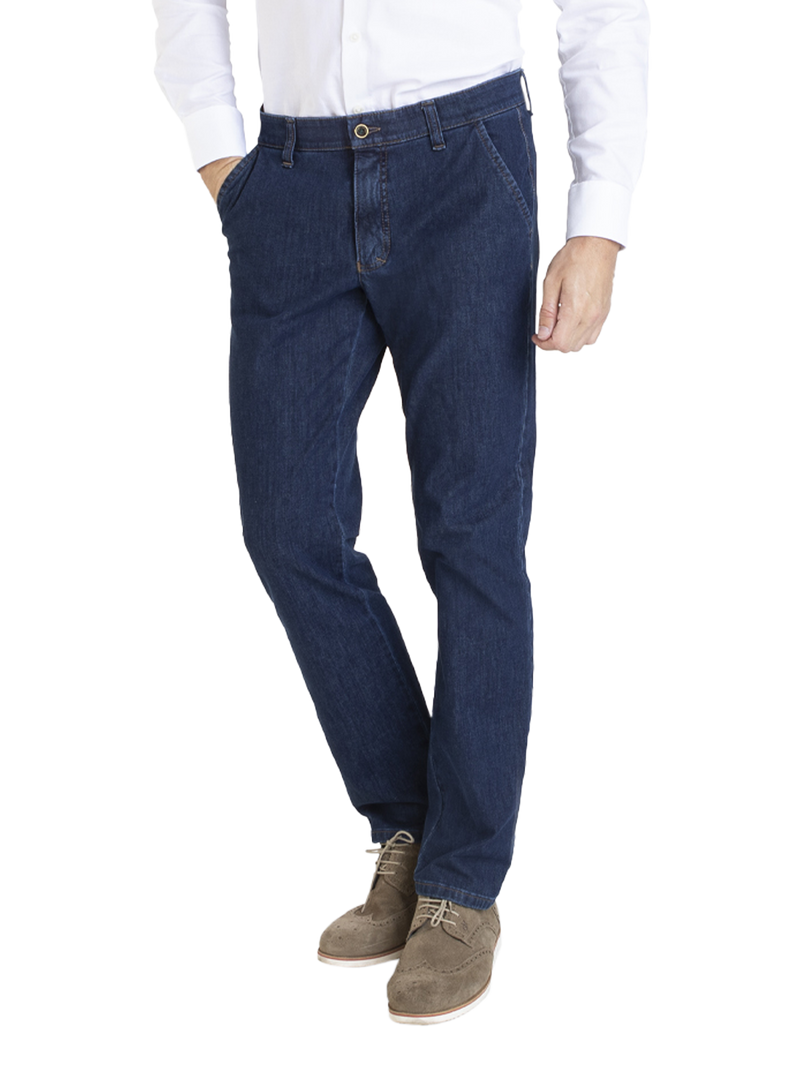 Mann trägt dunkle Jeans, die passgenau sitzen und leicht gerippt sind, kombiniert mit einem weißen Hemd und braunen Schuhen.