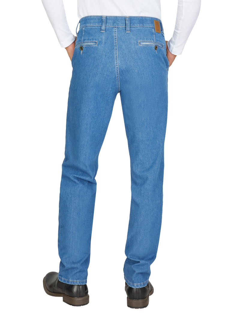 Blick auf die Rückseite eines Mannes, der eine weiße Hemd und hellblaue Jeans trägt. Die Jeans hat zwei Gesäßtaschen mit Reißverschluss, Gürtel- und Gürtelschlaufen sowie einen braunen Leder-Aufsatz am Bund. Er steht mit Händen in den Taschen.
