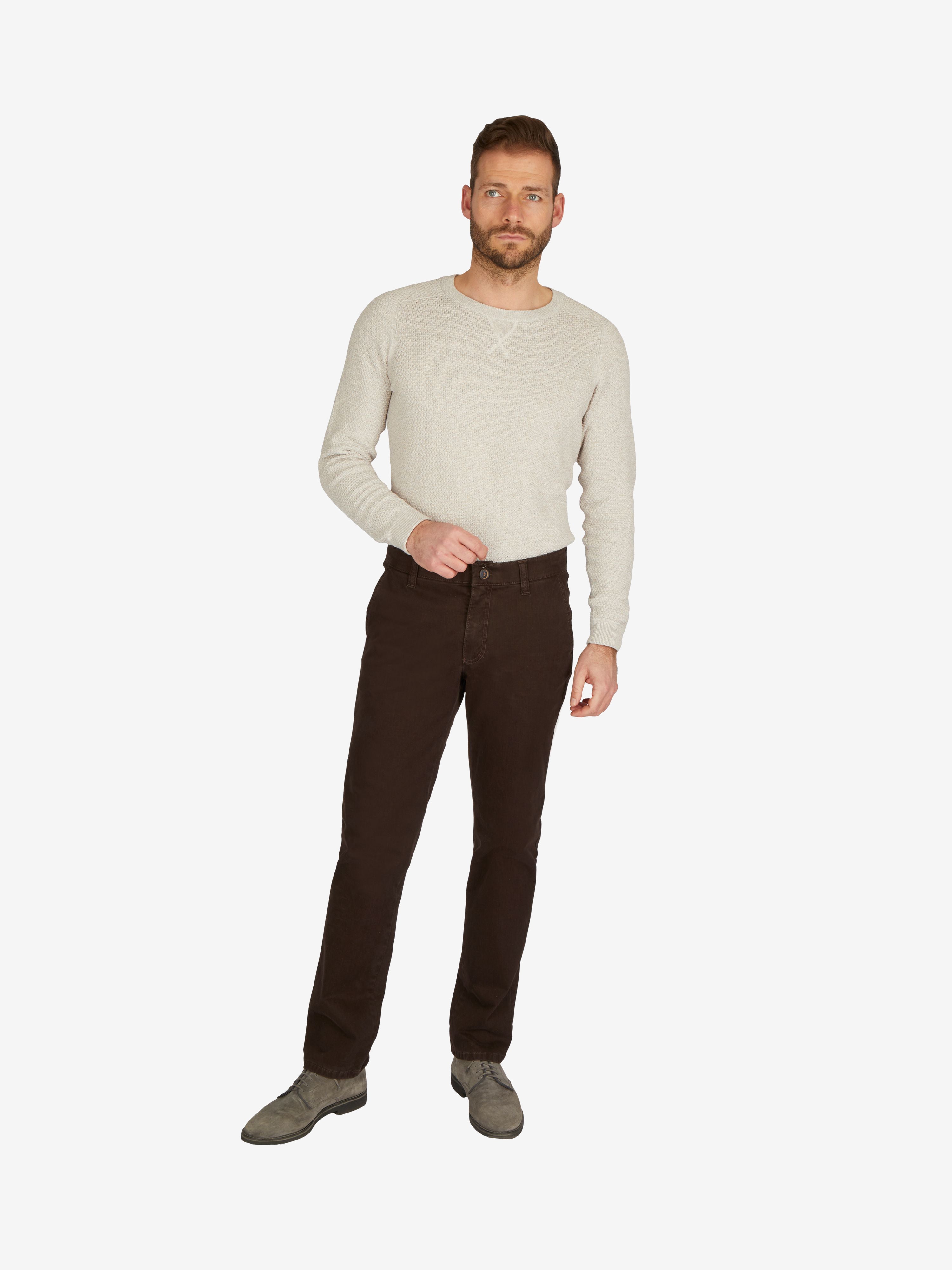 Männlicher Modell trägt dunkelbraune GARVEY 7612 Flat Front-Hose aus elastischer Baumwolle mit Komfortbund, Hemdenstopper und schmaler Fußweite, kombiniert mit cremefarbigem Pullover und grauen Schuhen.