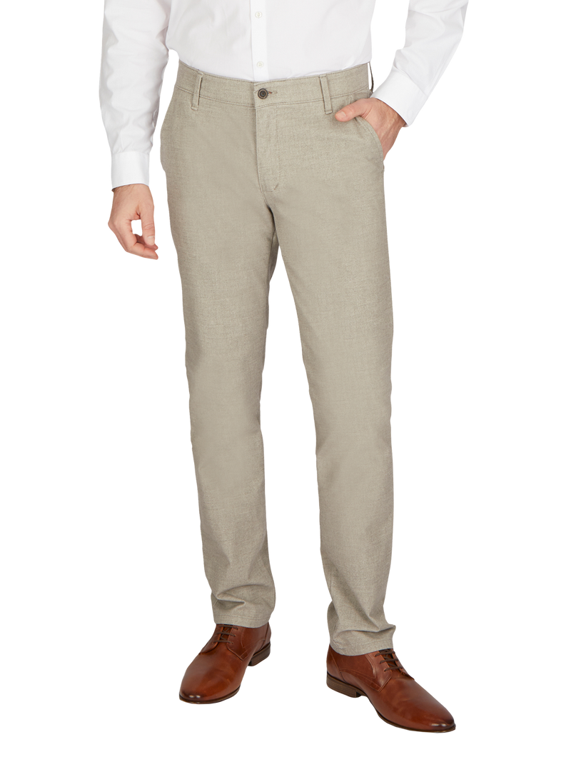 Nahaufnahme eines Mannes, der beige Stoffhose, weißes Hemd und braune Lederhalbschuhe trägt. Die Person steht mit einer Hand in der Hosentasche.