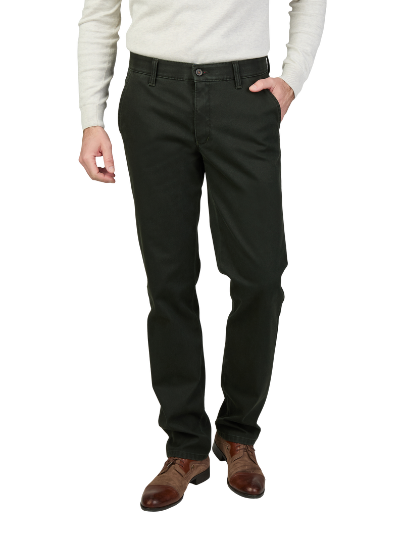 Hände in die Tasche steckende Person trägt schwarze Chino-Hose, beige Pullover, braune Lederstiefel. Der Fokus liegt auf den Hose und den Schuhen.