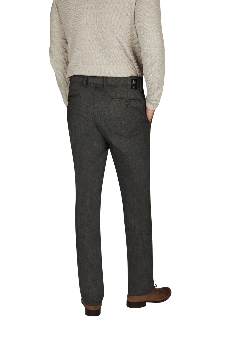 Nahaufnahme eines Mannes, der eine dunkelgraue Anzugshose und braune Lederschuhe trägt. Der Mann trägt außerdem einen hellen Pullover und hat eine Hand in der Hosentasche. Das Bild zeigt nur den unteren Rücken und die Beine des Mannes.