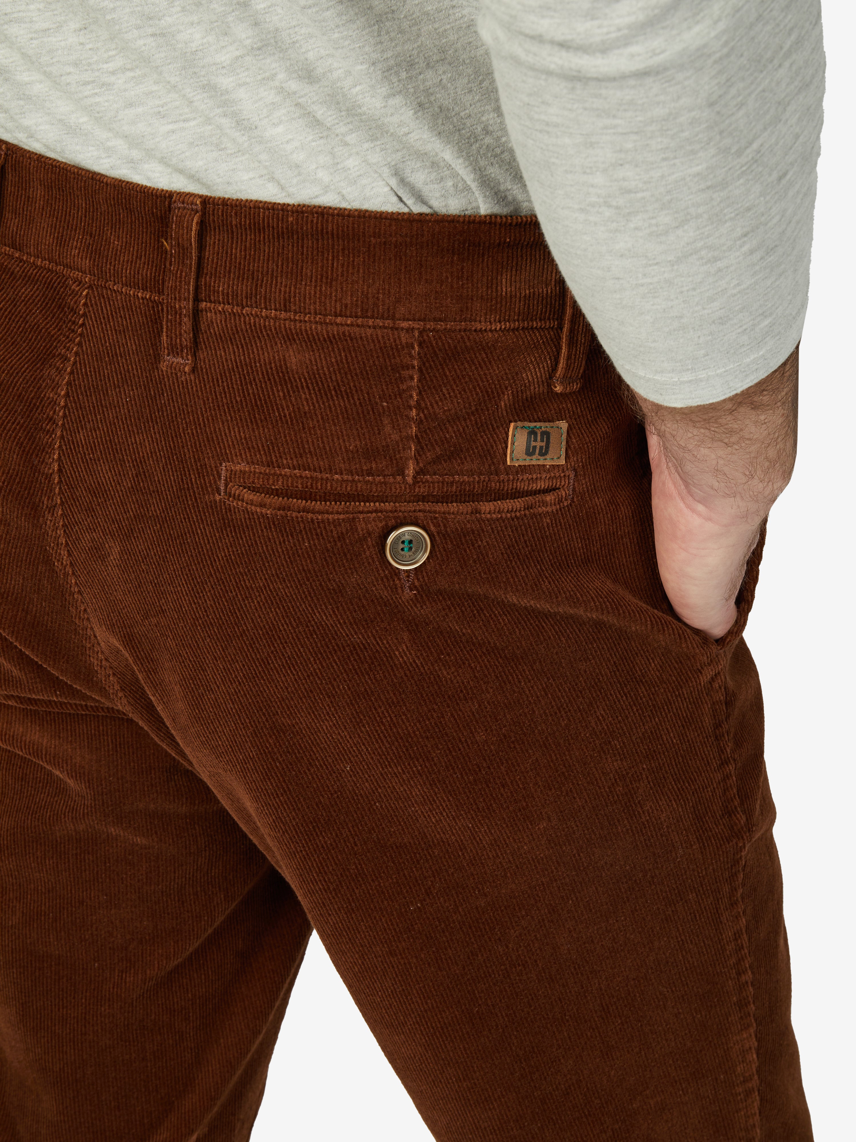 Nahaufnahme einer braunen Cord-Hose des Models, sichtbarer Hemdenstopper, Bund mit Knopf und Haken, einfache Seitentasche, Logo-Label am Bund, getragen mit einem hellgrauen Pullover, bequemer Flat Front-Stil, hochqualitative Verarbeitung, geeignet für Herbst/Winter.