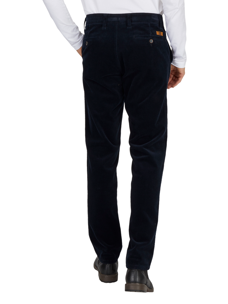 Herrenhose aus dunklem, weichem Cordstoff, getragen von einer Person, die eine weiße Hemd trägt. Die Hose hat eine normale Passform, seitliche Eingrifftaschen, hintere Taschen mit Knöpfen und eine kleine Leder-Logoplatte am Gürtel.