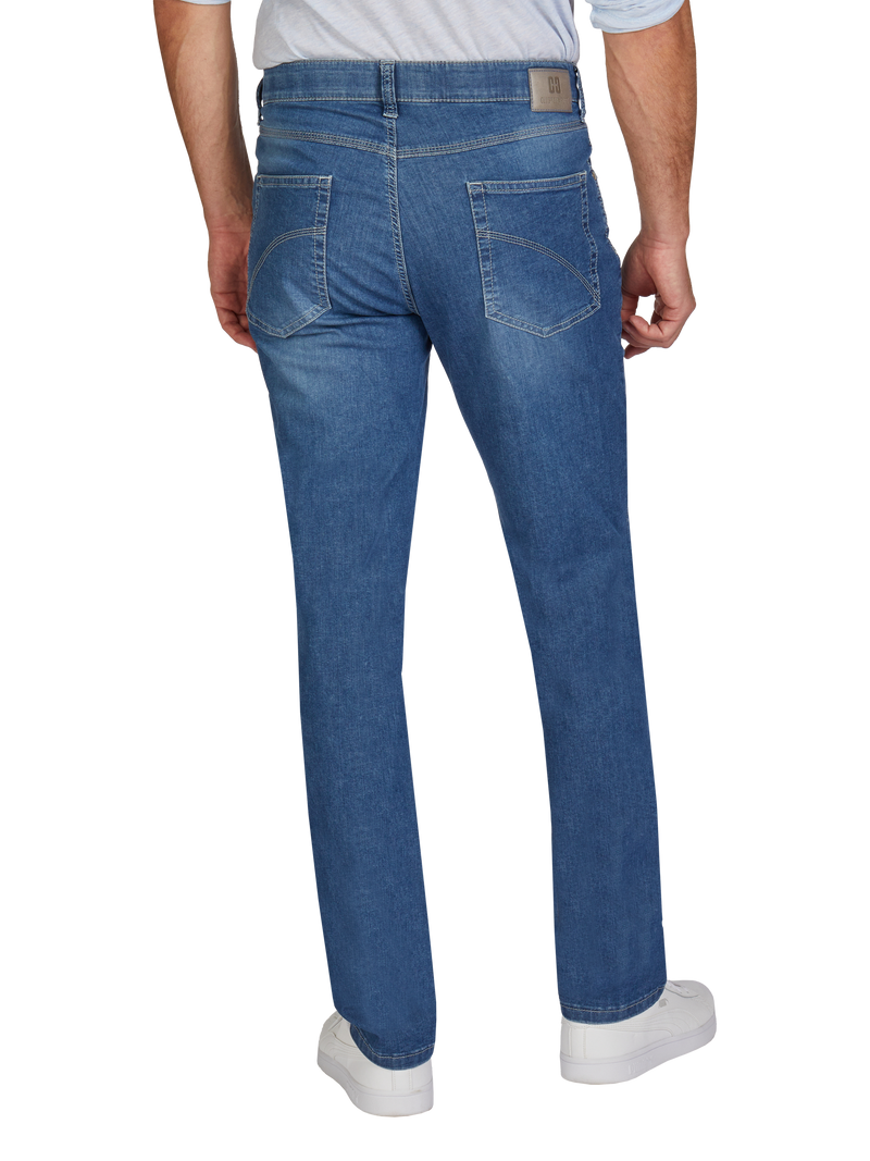 Blick auf die Rückseite eines Mannes, der blaue Jeans trägt. Die Jeans hat eine lockere Passform, zwei sichtbare Gesäßtaschen mit winkeliger Linienführung, einen braunen Lederetikett am Bund auf der rechten Seite und einen klassischen Denim-Farbton. Der Mann trägt weiße Sneakers.
