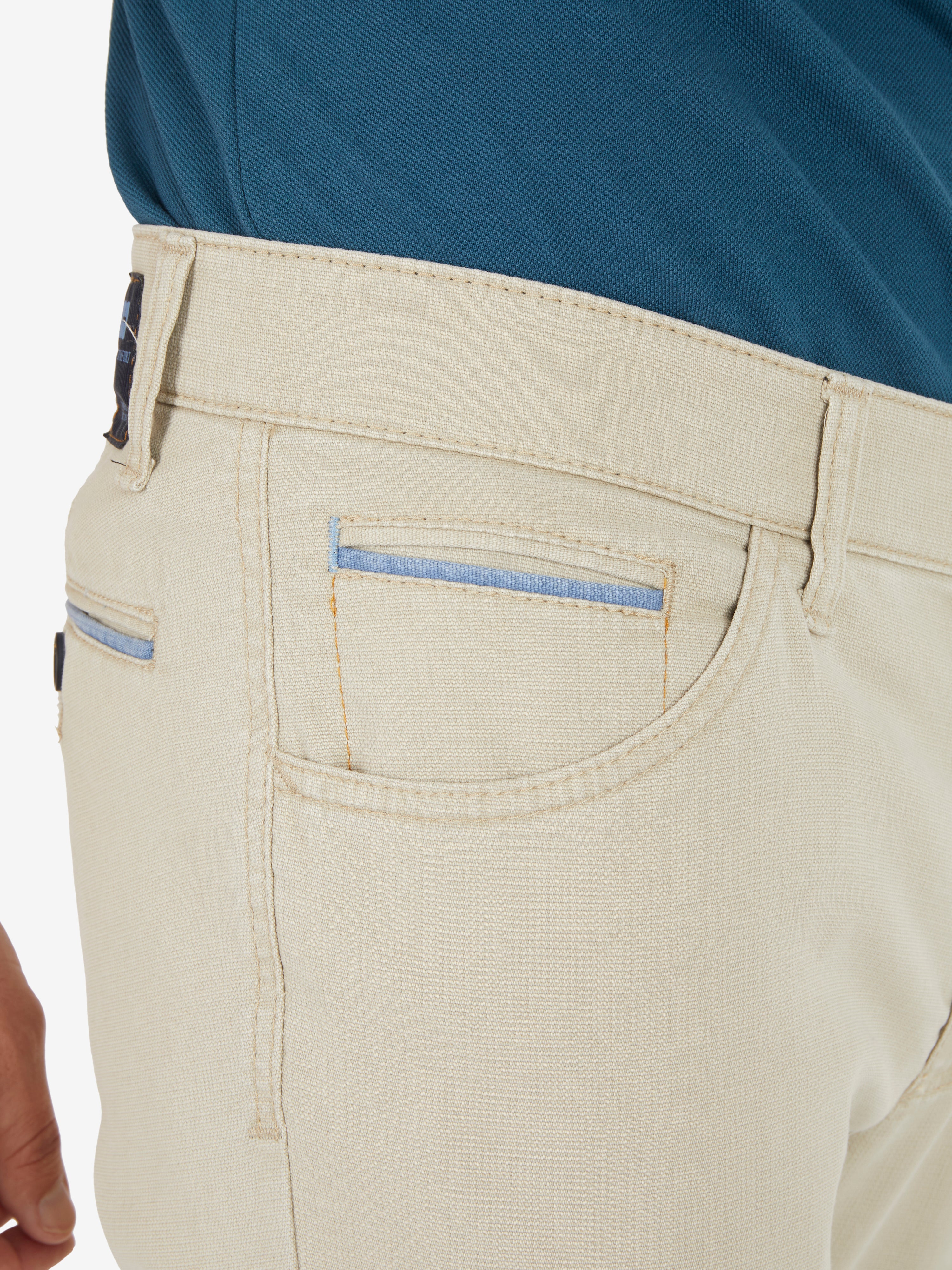 Nahaufnahme einer beige Hose, die MARVIN 7506 Modell von Club of Comfort zeigt. Die modifizierte 5-Pocket-Hose aus High Stretch-Baumwolle verfügt über einen Comfortbund, Hemdenstopper, Swing-Pockets mit Paspeln und Kontrastakzenten auf den Münztaschen. Das Bild hebt den elastischen Bund und die doppelt paspelierte Münztasche hervor.