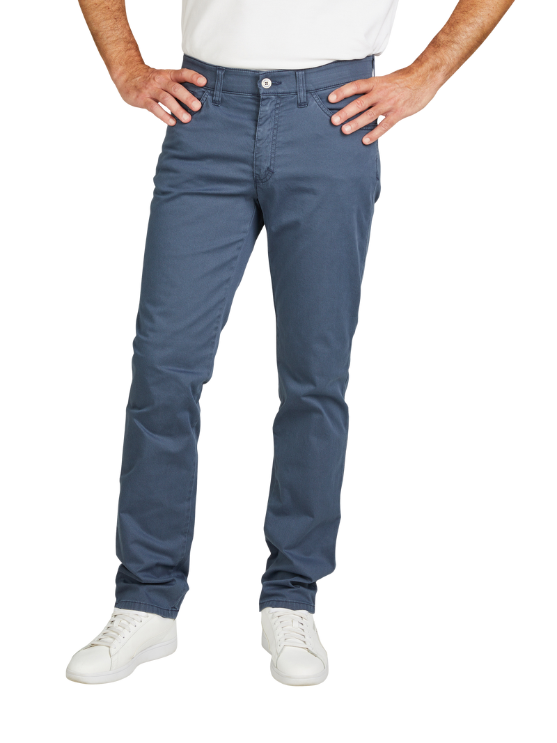 Der Bildausschnitt zeigt eine Person in weißen Sneakern, blauen Chino-Hosen und einem weißen Oberteil, die mit beiden Händen in die Hüften gestützt ist.