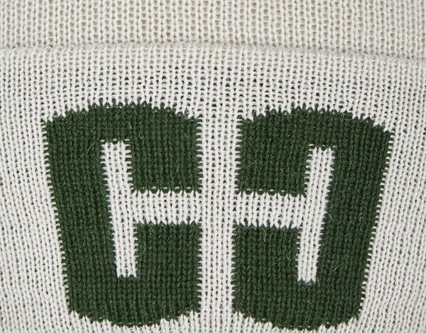 Nahaufnahme eines weißen Textilstoffes mit grünem, gedrucktem Symbol, das die Buchstaben "C" und "H" in gegengesetzten Richtungen zeigt. Das Symbol besteht aus groben, dicken Strichen, die deutlich sichtbar auf das Gewebe aufgedruckt sind.