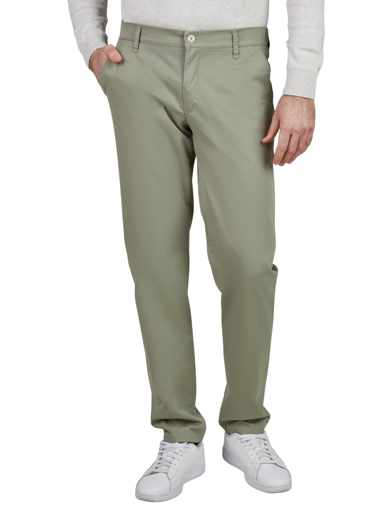 Blick auf eine Person im weißen Hemd und grauer Jacke, die hell grüne Chino-Hose trägt. Die Person hat eine Hand in der Tasche und trägt weiße Turnschuhe. Das Bild zeigt nur den unteren Teil des Körpers, Beine und Füße.