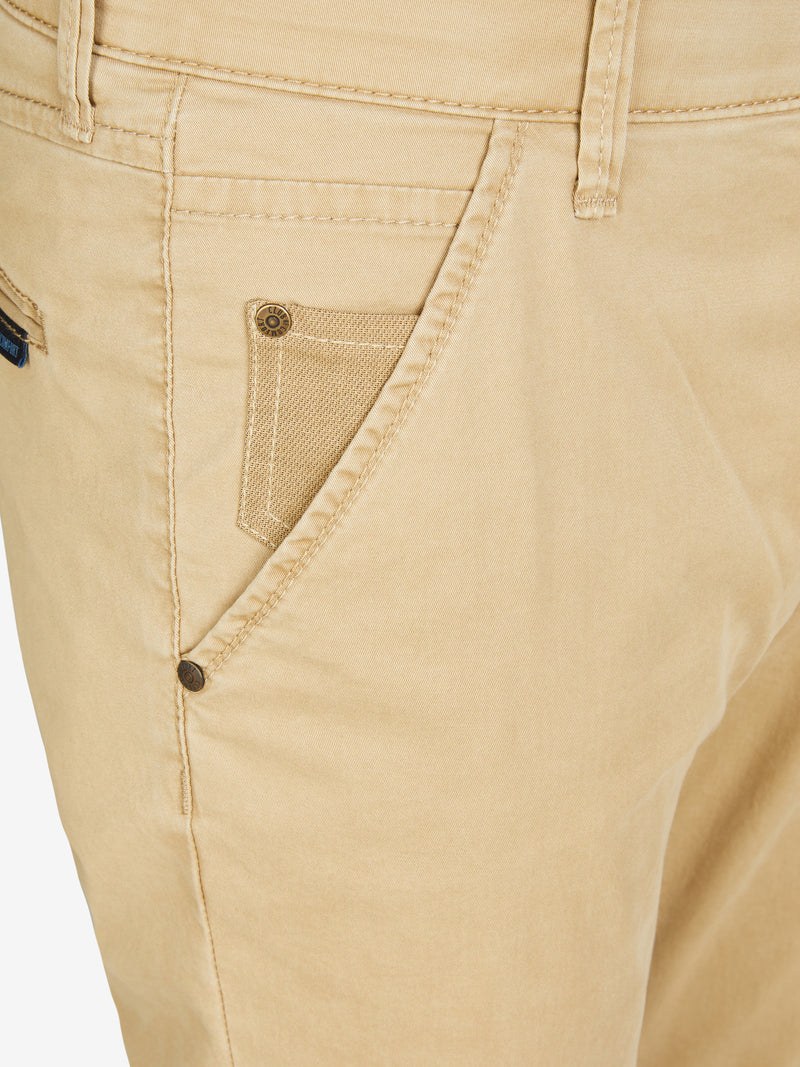 Nahaufnahme einer beigen Chino-Hose (PHIL 7708), mit elastischem Comfortbund, Hemdstopper und Münztasche, gefertigt aus leichtem Baumwoll-High-Stretch-Material. Die Hose hat eine Slim Fit Passform, normale Leibhöhe und schmale Beinweite.