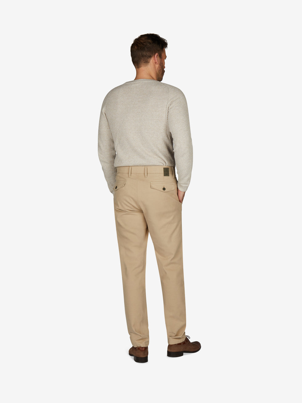 Mann trägt eine hellbeige Chinohose im Tapered Fit mit Komfortbund und Hemdenstopper, gefertigt aus High Stretch Baumwolle. Die Hose hat eine normale Leibhöhe, mehr Platz im Gesäß- und Oberschenkelbereich, einen schmalen Beinverlauf und ist ideal für Herbst/Winter.