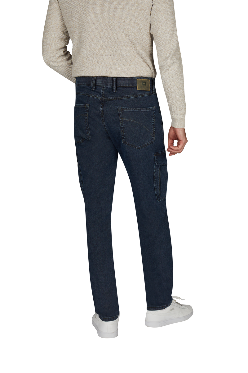 Ein Mensch steht mit dem Rücken zur Kamera und trägt eine beige, langärmlige Jacke, dunkle Jeans mit sichtbaren Nähten und Taschen, weiße Sneakers.