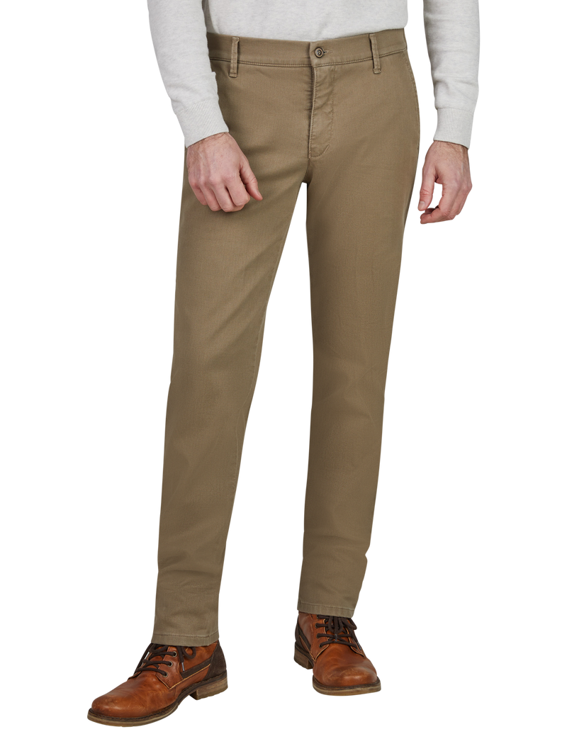 Blick auf eine Person, die khaki-farbene Chino-Hose trägt, die bis zu den Knöcheln reicht. Die Hose hat Gürtelschlaufen, einen Knopf und einen Reißverschluss. Die Person trägt braune Lederstiefel und ein hellgraues Oberteil.