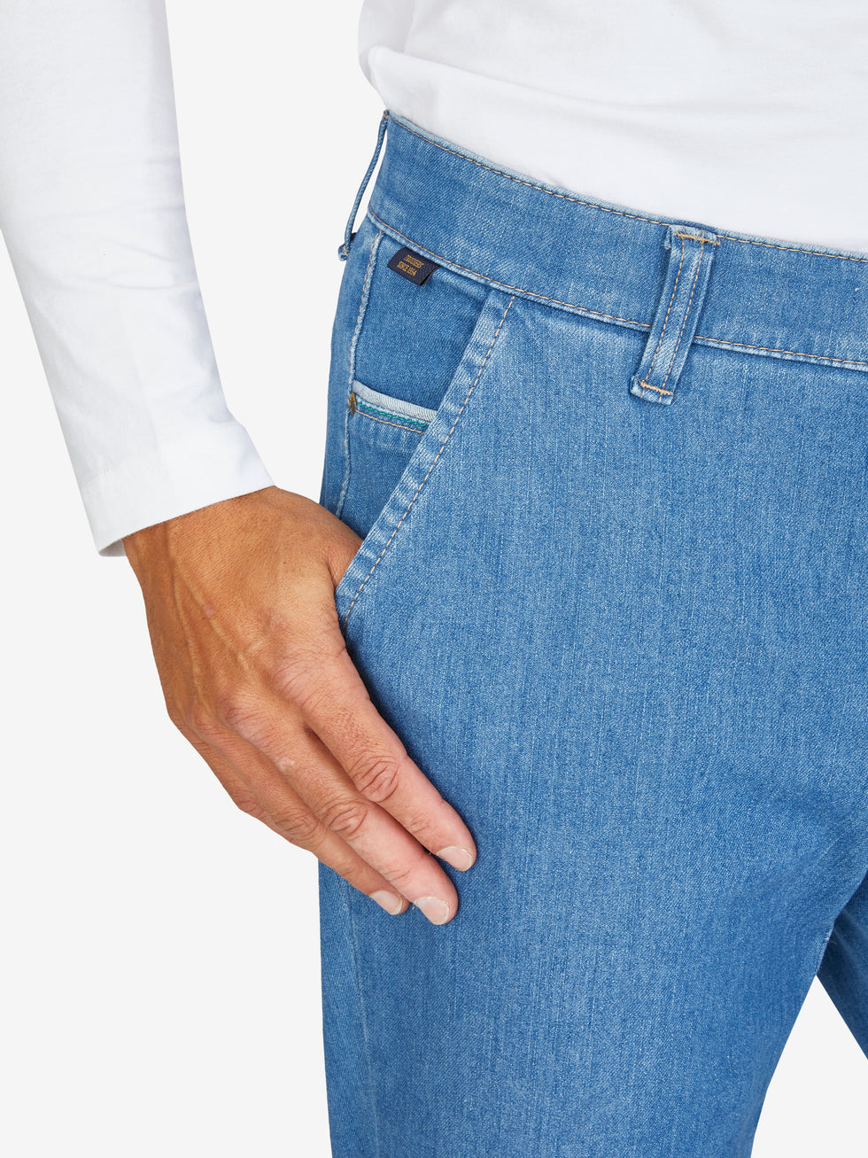 Hose aus hellblauem Bi-Stretch-Denim mit Flat Front, elastischem Komfortbund und Hemdstopper, rechte Münztasche, schmaler Beinverlauf, normale Leibhöhe, getragen von einer Person in weißem Oberteil, Produkt von GARVEY/Club of Comfort.