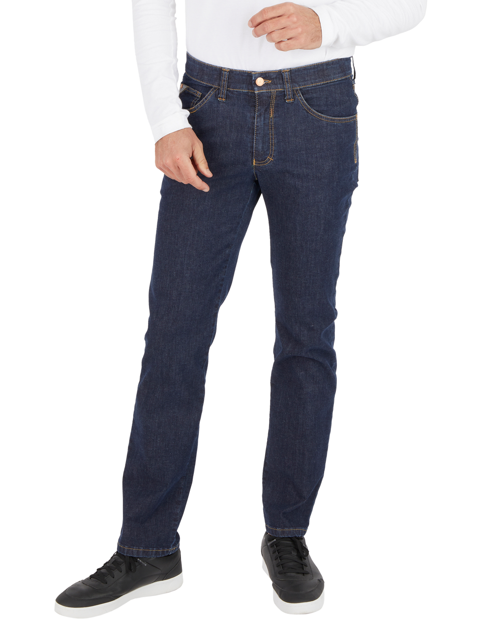 Nahaufnahme einer Person in dunklen Jeans, mit weißem Oberteil und schwarzen Sportschuhen, die locker eine Hand in die Tasche steckt.