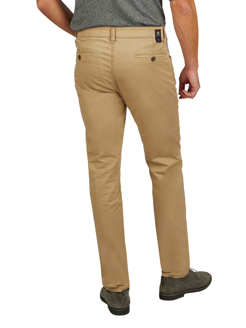 Blick auf die Rückseite einer Person, die beige Chino-Hosen trägt, die leicht sitzen. Die Person steht aufrecht, eine Hand ist an der Seite, die andere ist am Rücken. Die Hosen haben Gürtelschlaufen, eine kleine schwarze Label am Bund und zwei eingearbeitete Gesäßtaschen. Die Schuhe sind dunkel, und die Person trägt ein graues Oberteil.