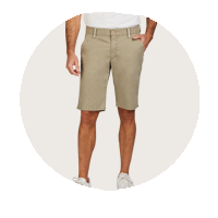 Mann mit einem beigefarbigen Shorts, das bis über die Knie reicht, und weißem T-Shirt. Er trägt weiße Sneakers und hat eine Hand in der Tasche.